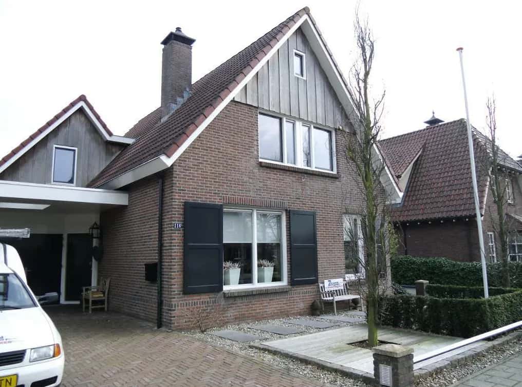 Vrijstaande woning met donkere luiken en kozijnen na buitenschilderwerk, met het bord van Zigahn Schilderwerken in de voortuin